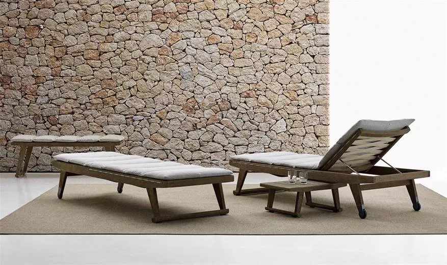 B&B Italia Gio Sonnenliege 200 cm mit Rollen verstellbar auf einem Teppich vor einer Steinwand mit einem Beistelltisch und zwei Gläsern.