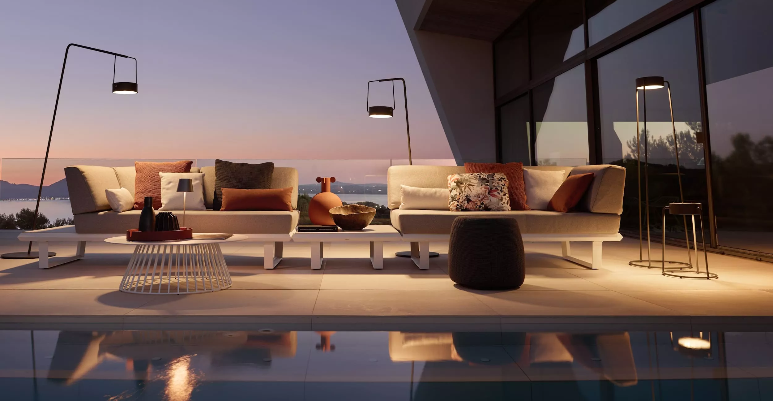 Solpuri Boom Lounge Set auf einer modernen Terrasse bei Sonnenuntergang mit stilvollen Kissen und Beleuchtung im Hintergrund.