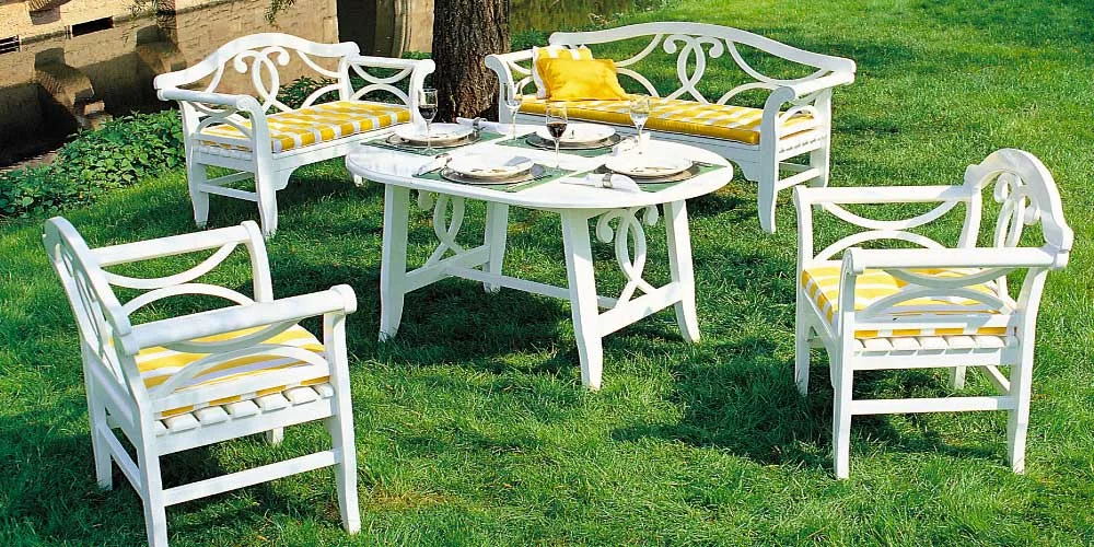 Herrenhaus Nicole Essgruppe in Weiß mit gelben Kissen auf einer grünen Wiese, bestehend aus Tisch, zwei Stühlen und zwei Bänken.