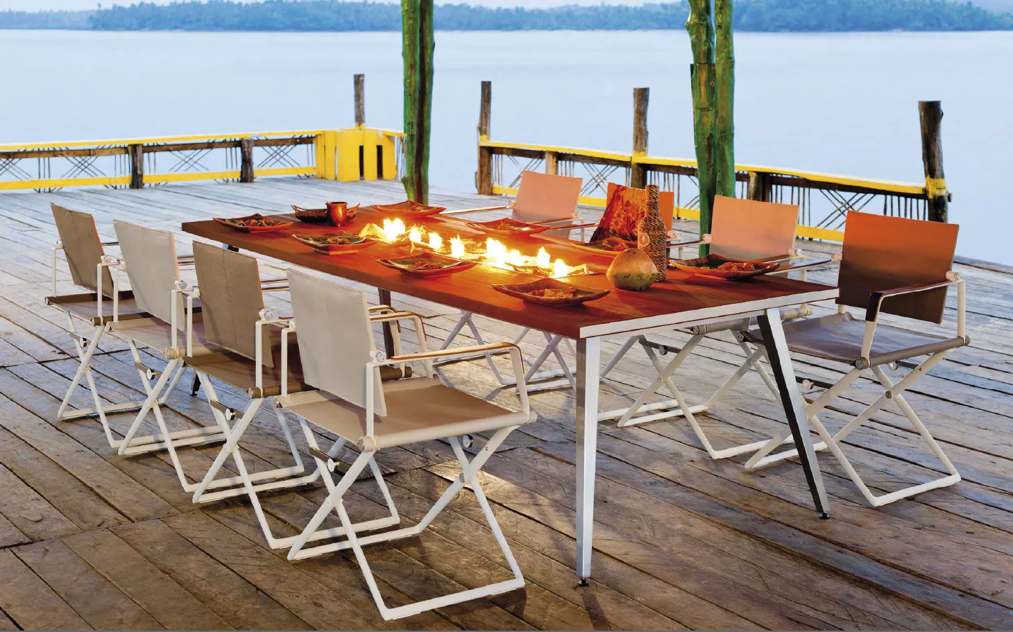 Dedon Seax Kollektion Seax Armlehnstuhl klappbar in einer Outdoor-Szene mit gedecktem Tisch und Stühlen auf einer Terrasse am Wasser