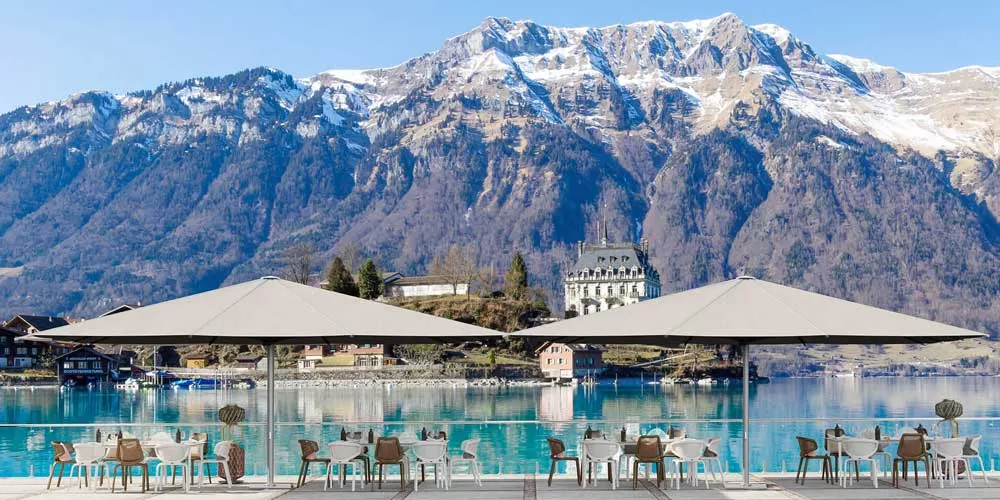 Glatz Gastronomie Sonnenschirme Palazzo Royal in Beige vor malerischer Bergkulisse und See, ideal für Outdoor-Cafés.