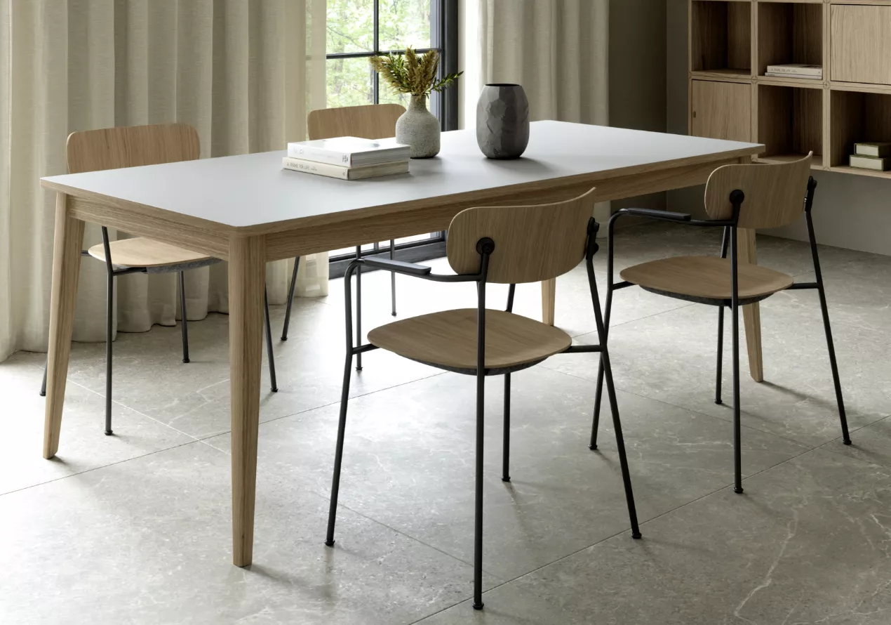 Esszimmer mit SCOPE Kollektion: Holztisch mit weißer Platte, vier Holzstühlen, Vase und Pflanzen, vor bodenlangen Vorhängen.