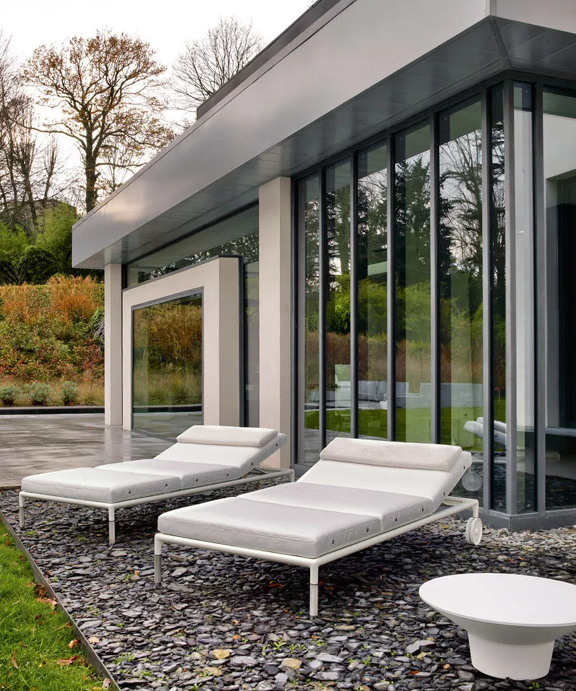 B&B Italia Springtime Outdoor Beistelltisch 43 steht neben zwei weißen Sonnenliegen vor einem modernen Haus mit großen Glasfenstern 