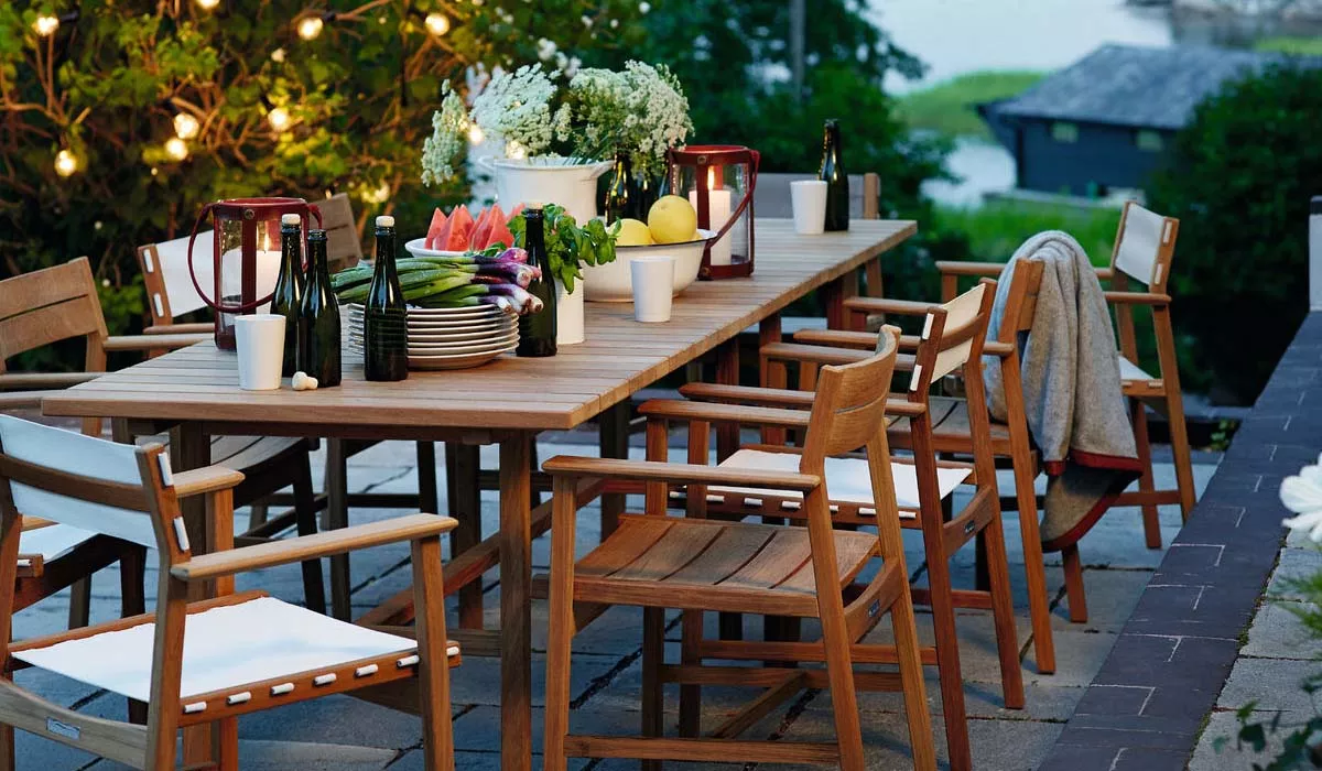 Skargaarden Sitzmöbel in Holzoptik auf einer Terrasse, umgeben von Lichterketten und gedecktem Tisch mit Geschirr und Blumen.