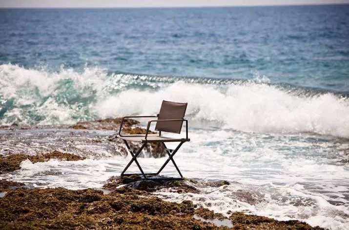 Dedon Seax Armlehnstuhl aus der Seax Kollektion steht auf Felsen am Meer während die Wellen im Hintergrund brechen Mood Bild