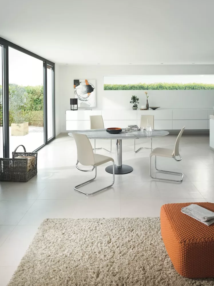 Esszimmer mit Draenert Titan Tisch und weißen Stühlen in modernem Ambiente mit großen Fenstern und Blick auf den Garten 