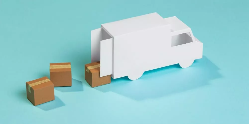 Ein weißer Papier-LKW mit drei kleinen braunen Kartons auf hellblauem Hintergrund, symbolisiert Versandinformationen.