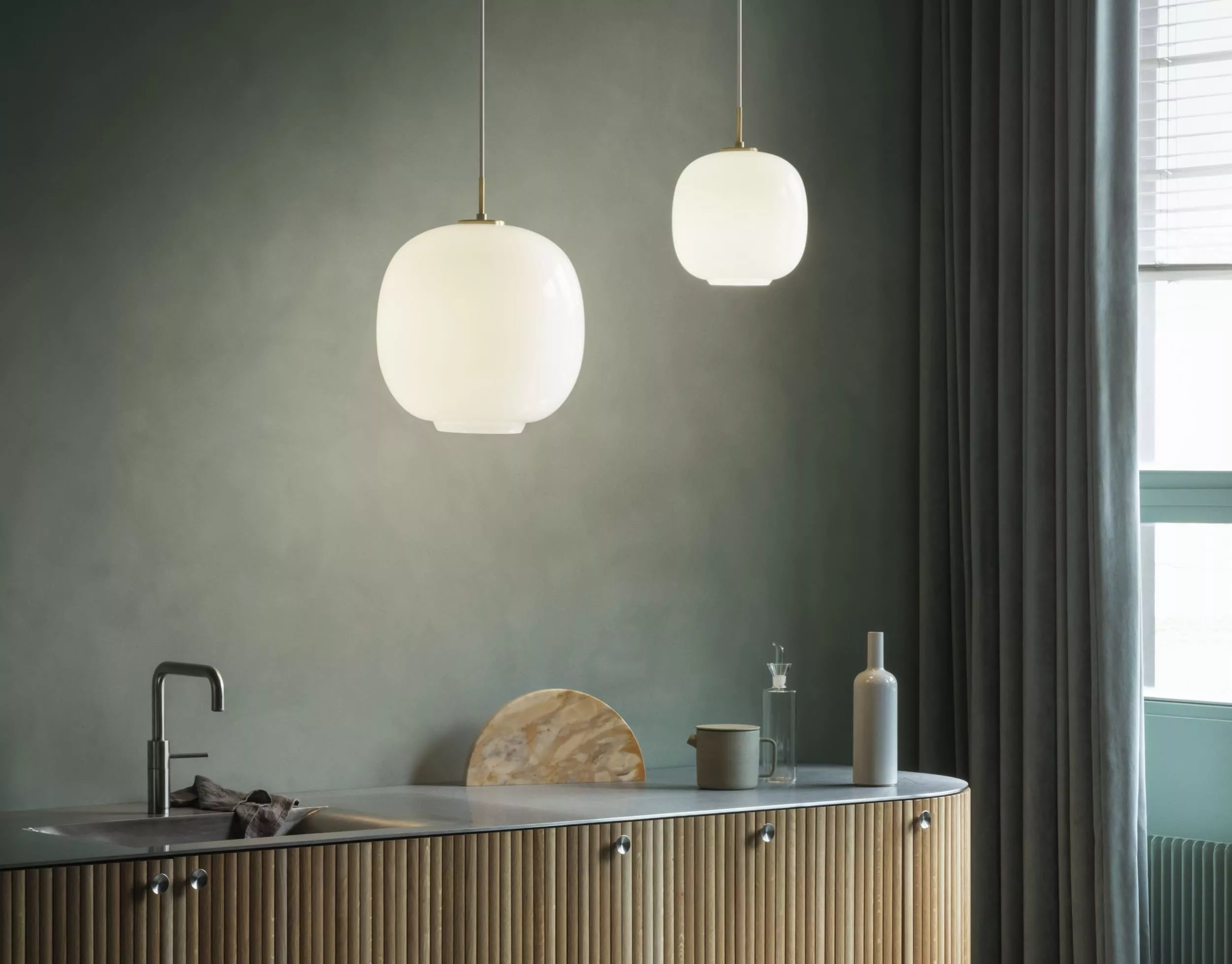 Zwei weiße Louis Poulsen VL45 Pendelleuchten hängen in einer modernen Küche mit grauem Hintergrund und Holzdetails.