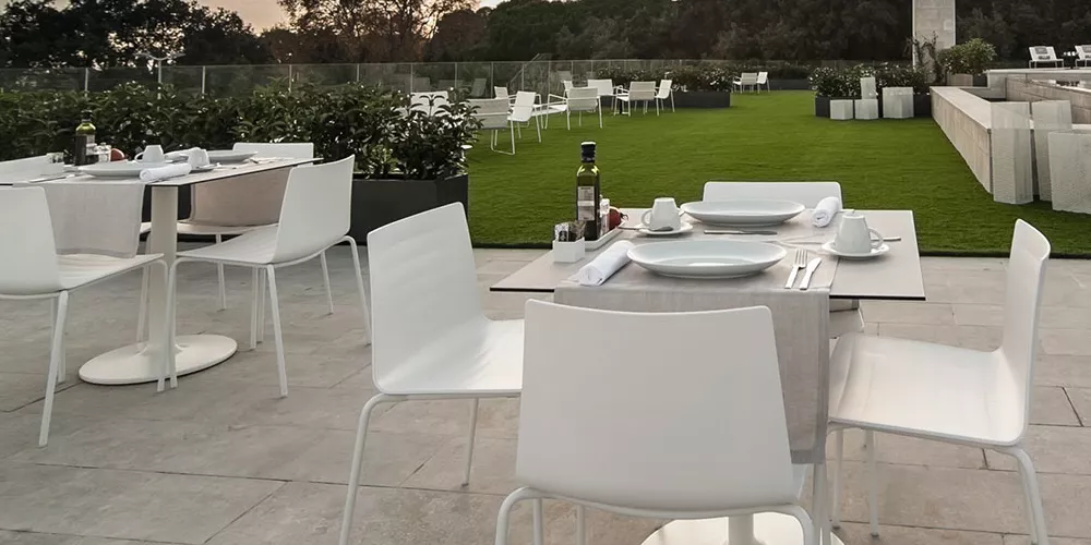 Andreu World Flex Stühle in Weiß auf einer Terrasse mit grünem Rasen und gedeckten Tischen bei Sonnenuntergang.