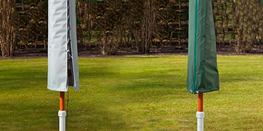 Zwei Schirmhauben von Villa Schmidt, eine in Grau und eine in Grün, auf einem Rasen vor einer Hecke, als Stimmungsbild.