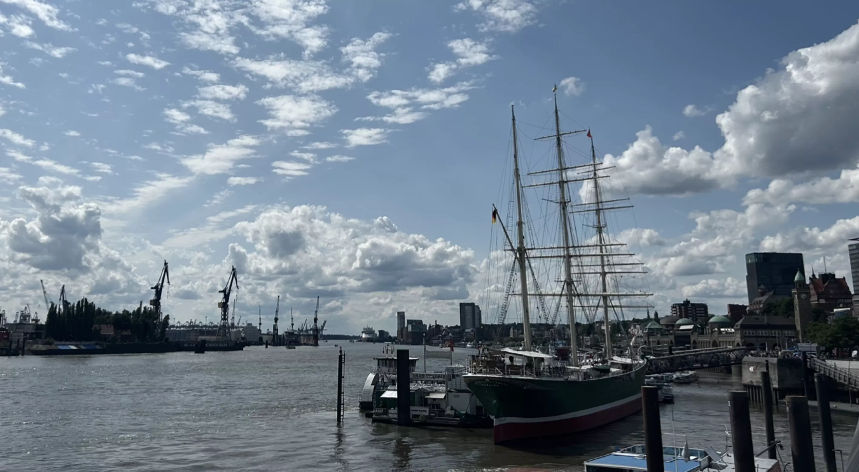 Ein Segelschiff liegt im Hamburger Hafen vor Anker, umgeben von Wasser und Wolken unter einem blauen Himmel.