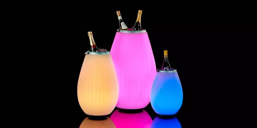 Drei leuchtende Joouls 3in1 LED-Kühler in Pink, Gelb und Blau auf schwarzem Hintergrund, gefüllt mit Flaschen, stimmungsvolle Produktpräsentation.