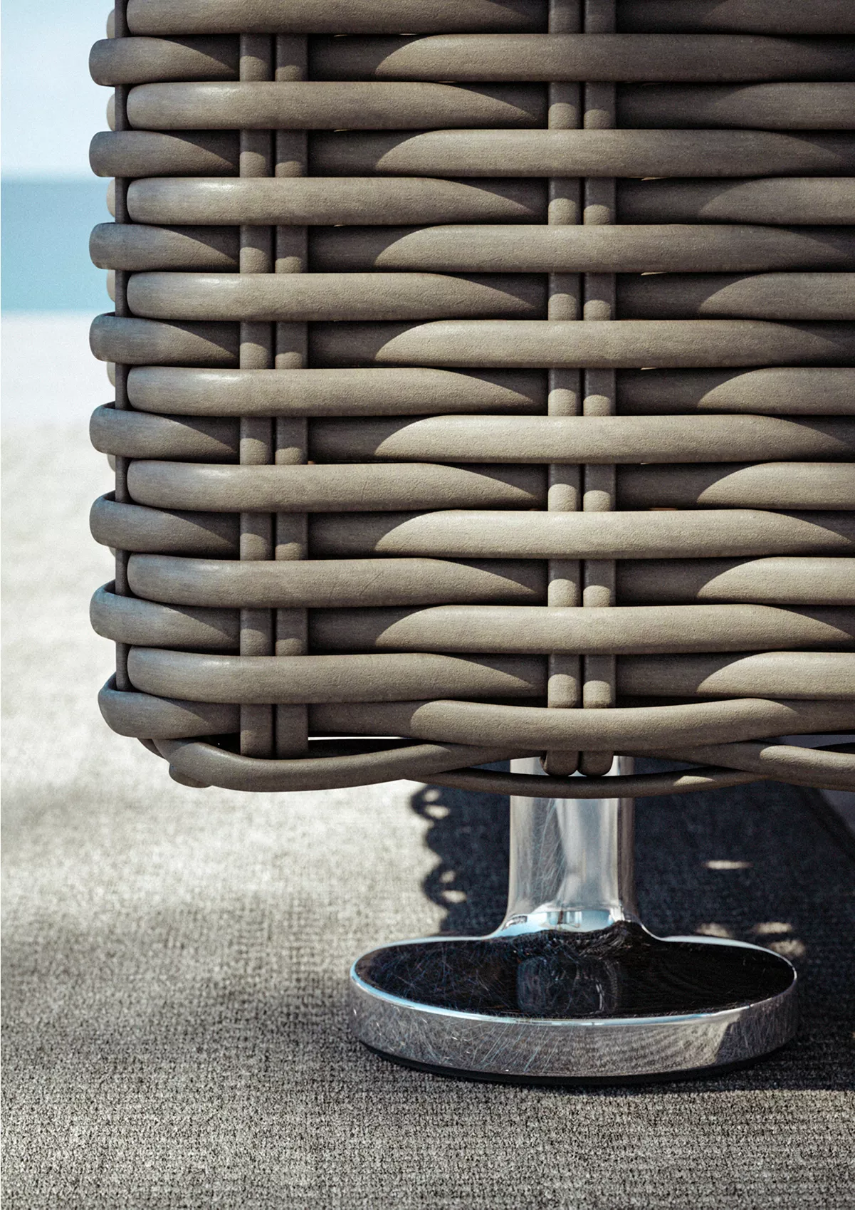 Detailaufnahme des Dedon Paros Gartenmöbels zeigt die hochwertige Flechtarbeit und den glänzenden Metallfuß auf einer Terrasse mit Meerblick