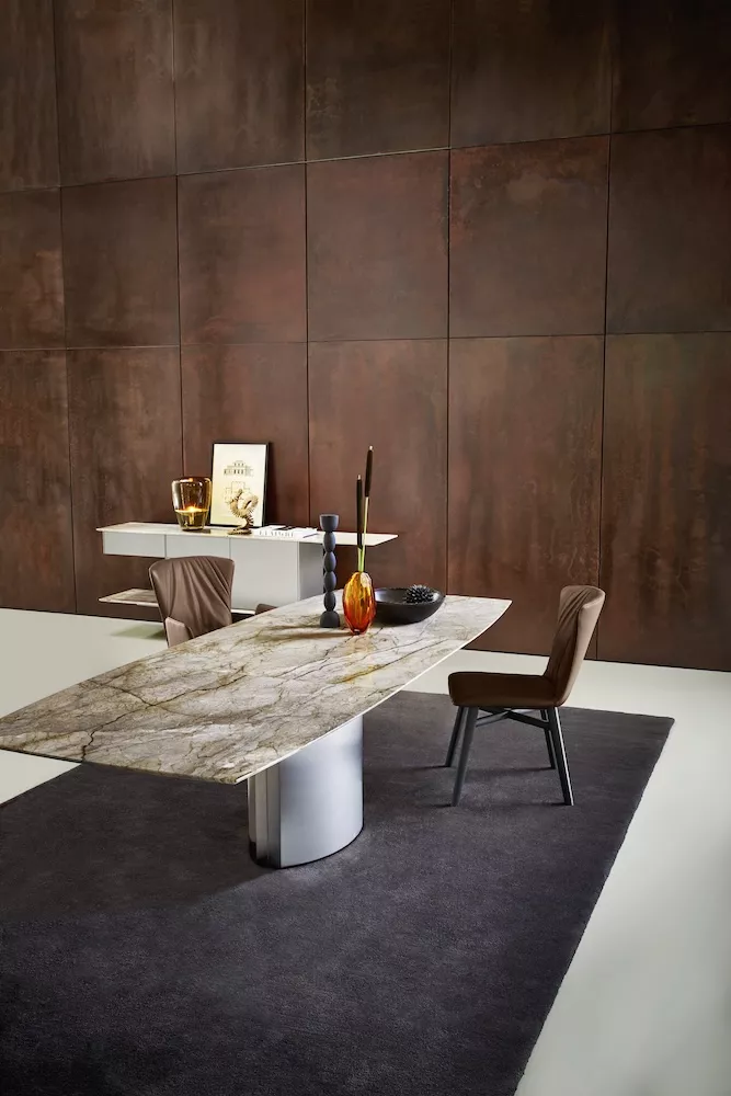 Der ADLER Tisch von DRAENERT steht in einem modernen Raum auf einem dunklen Teppich mit Dekorationsgegenständen im Hintergrund.