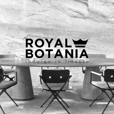 Schwarz-weißes Stimmungsbild von Royal Botania mit einem eleganten Outdoor-Tisch und Stühlen vor einer Steinwand.