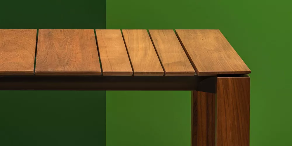 Andreu World Wind Tisch in Holzoptik, Detailansicht vor grünem Hintergrund, zeigt die elegante Maserung und Verarbeitung.