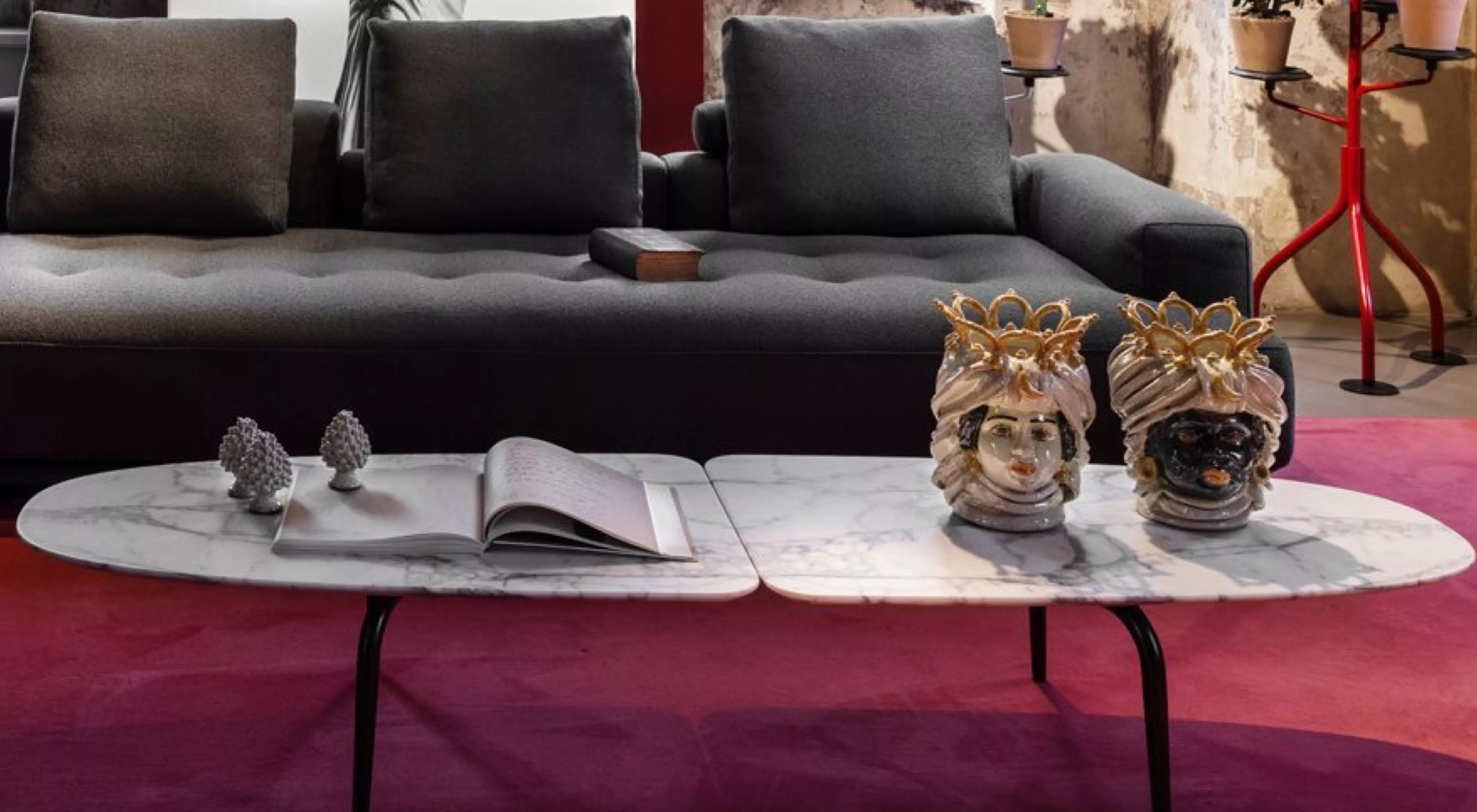 Zanotta Graphium Couchtisch in Marmoroptik vor einem grauen Sofa auf rotem Teppich, dekoriert mit Keramikfiguren und einem offenen Buch.