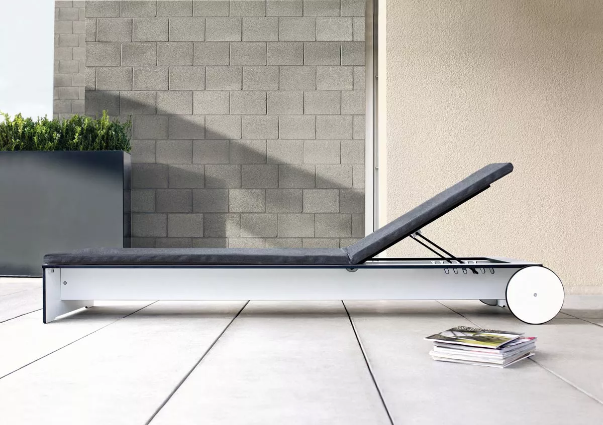 Sonnenliege Conmoto Riva in Grau, 70x216 cm, auf einer Terrasse mit modernen Pflanzkübeln und Zeitschriften im Vordergrund.