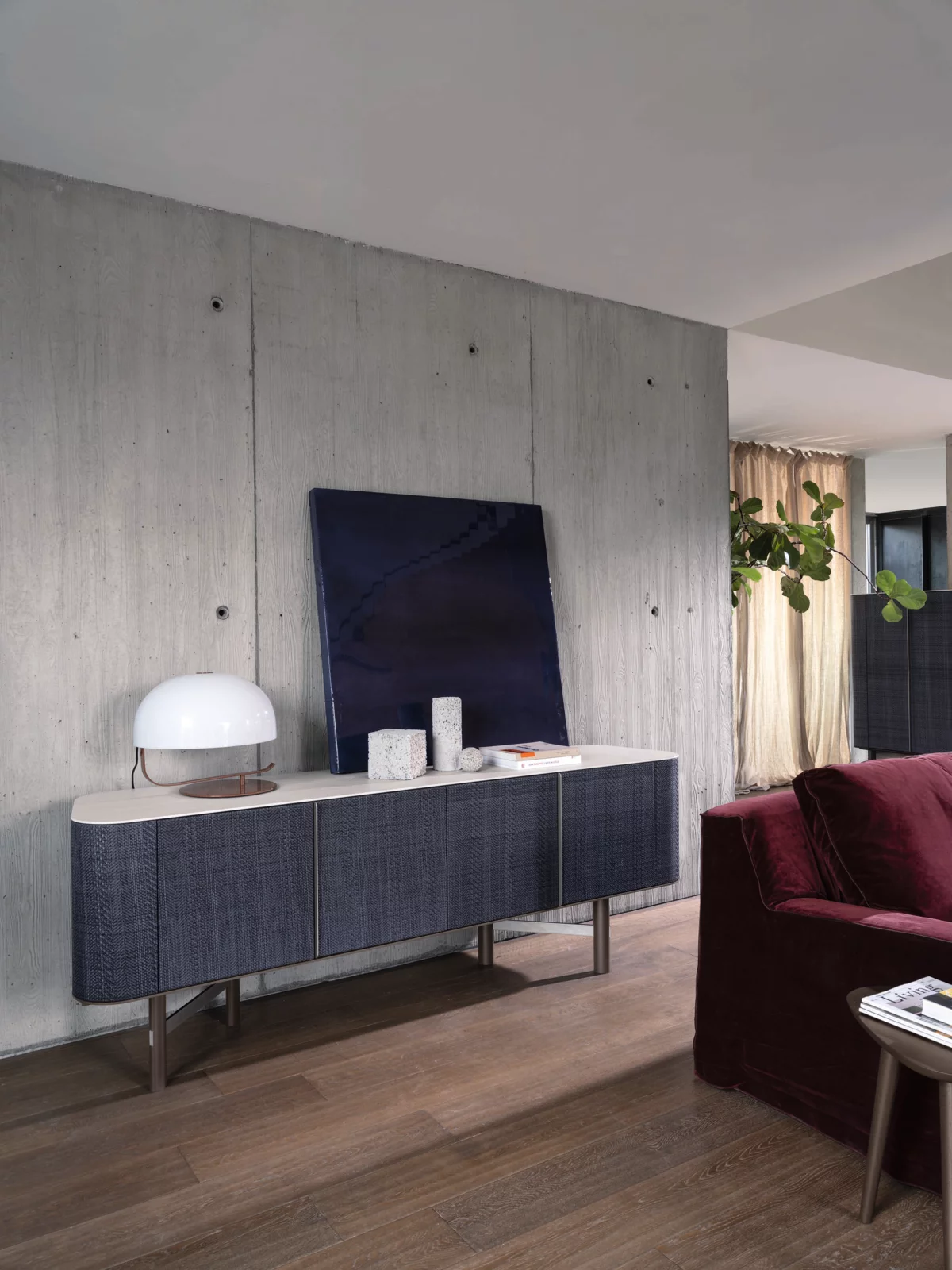Gervasoni Sideboard mit Dekorationen und Lampe in modernem Wohnzimmer mit Betonwand und rotem Sofa 