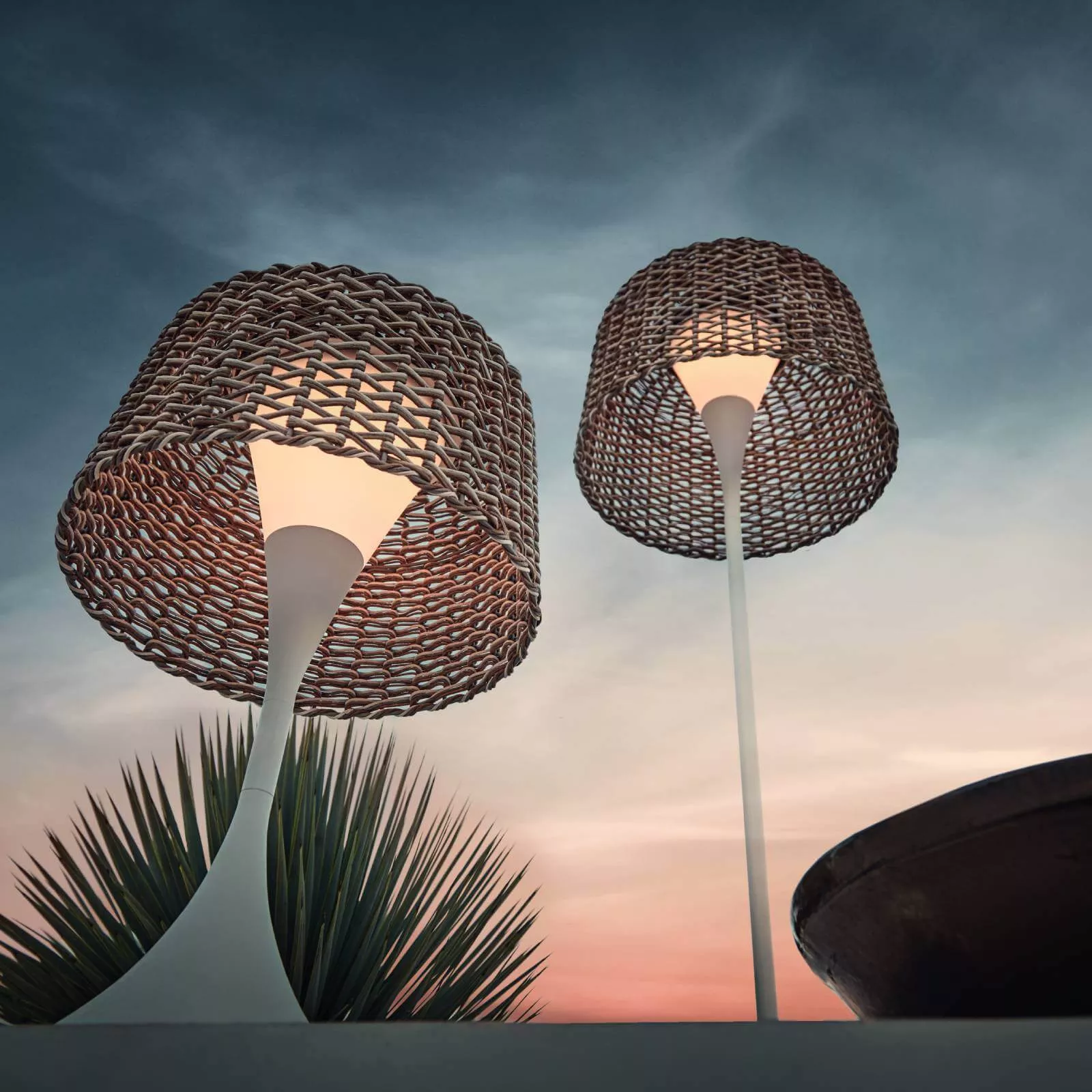 Zwei Gloster Ambient Mesh Leuchten in Weiß mit geflochtenem Schirm vor einem stimmungsvollen Abendhimmel.