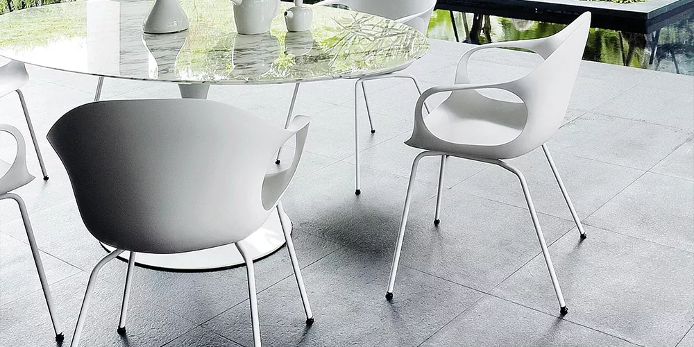 Kristalia Elefant Stuhl in Weiß, modernes Design, auf grauem Fliesenboden neben einem runden Glastisch, im Hintergrund Gartenblick.