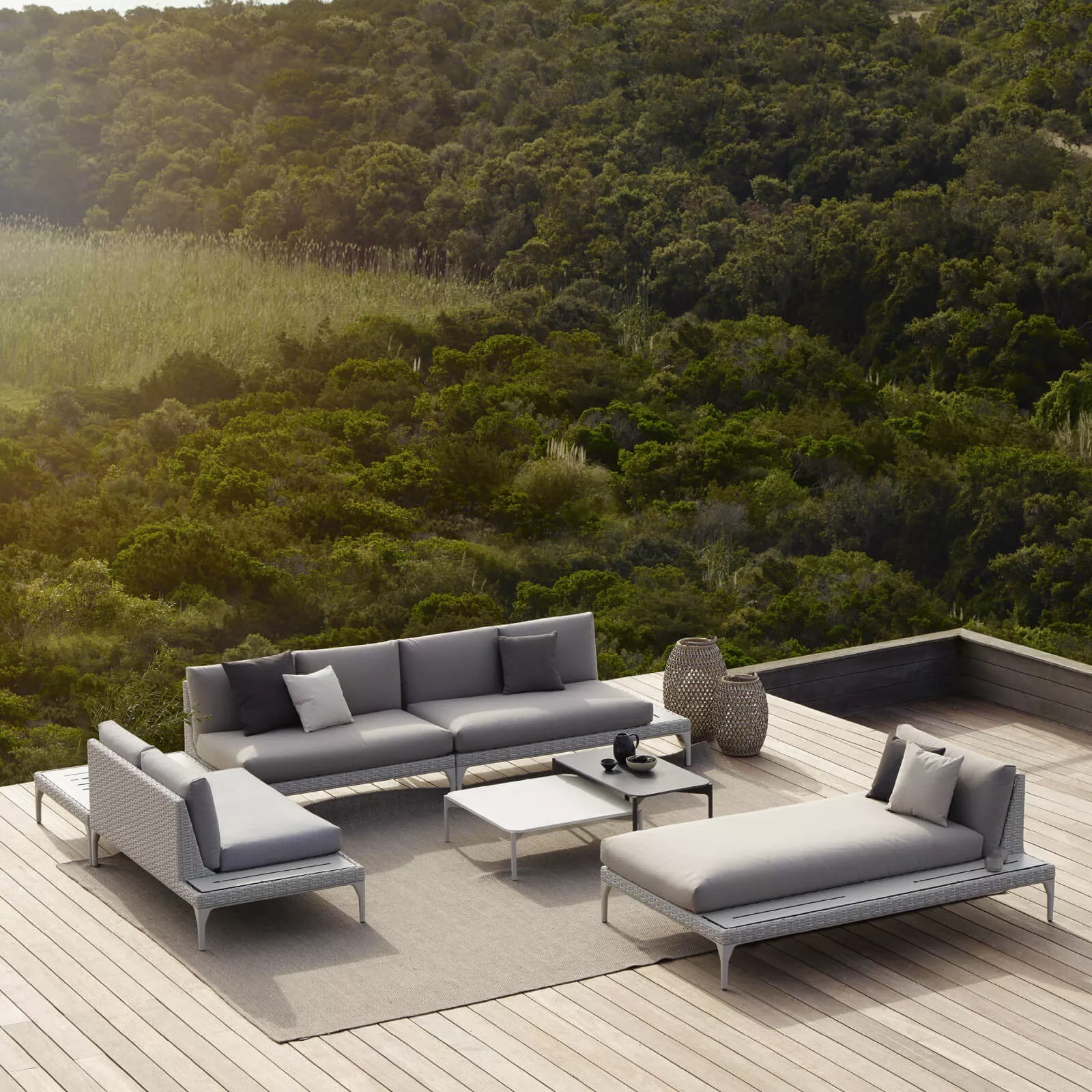 Dedon Izon Kollektion auf einer Terrasse mit Blick auf eine grüne Landschaft bestehend aus Sofas einem Tisch und einer Liege in einer entspannten Atmosphäre