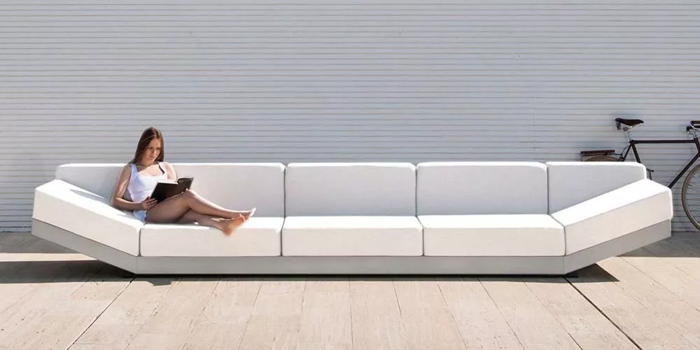 Frau sitzt auf einem weißen Calma Alat Sofa vor einer weißen Wand, mit einem Fahrrad im Hintergrund, in einer entspannten Atmosphäre.