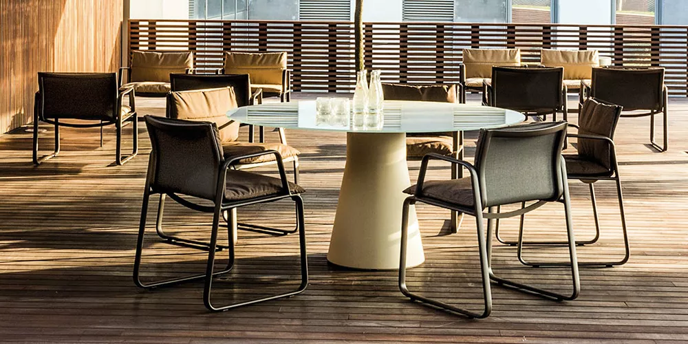 Andreu World Aire Stühle in Schwarz um einen runden Tisch auf einer Holzterrasse bei Tageslicht, mit Glasflaschen als Dekoration.