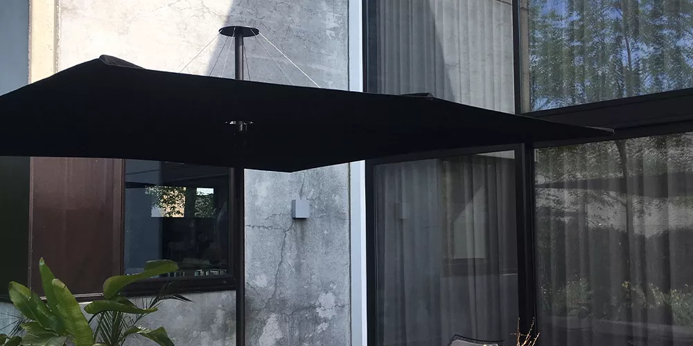 Sonnenschirm Infina von Umbrosa in Schwarz vor einer modernen Betonfassade im Garten.