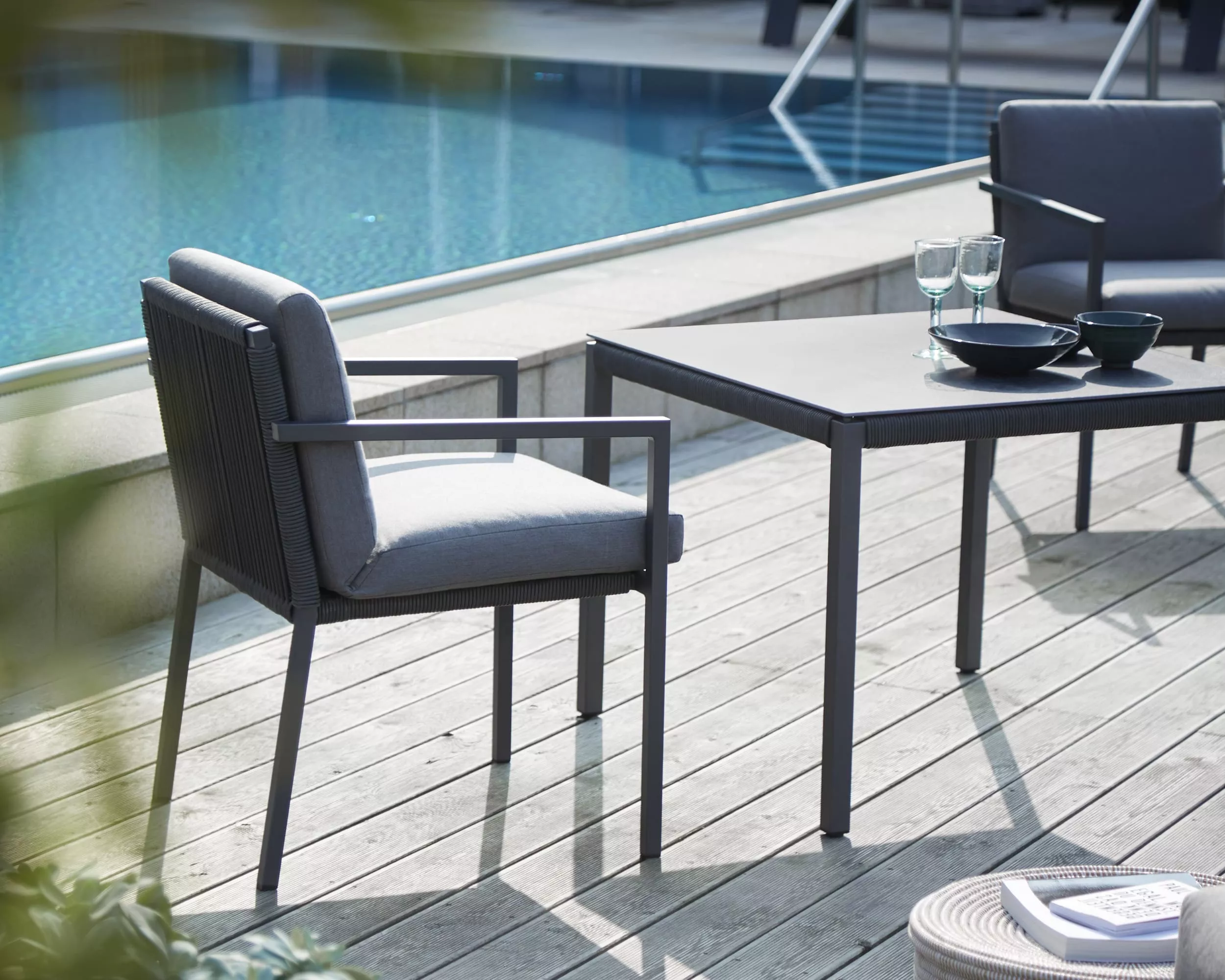 Solpuri Club Stuhl und Tisch stehen auf einer Terrasse am Pool mit zwei Gläsern und Schalen auf dem Tisch im Hintergrund ist Wasser zu sehen