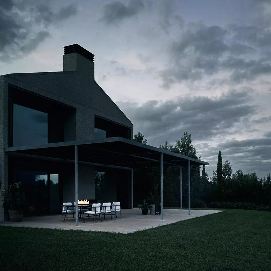 Ein modernes Haus mit großer Terrasse und B&B Italia Borea Loungesofa und Outdoor Loungegruppe bei Dämmerung im Garten.