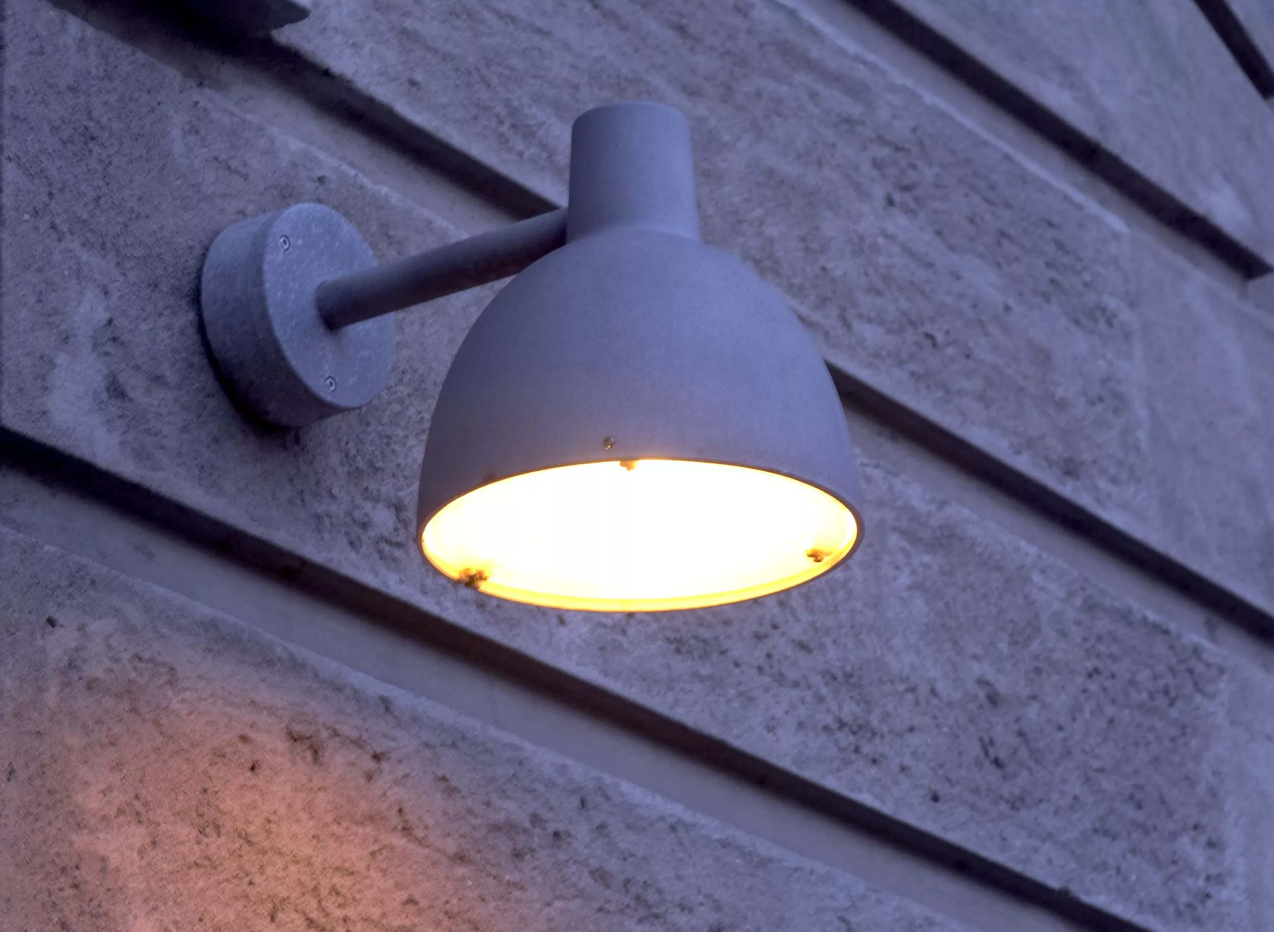 Außenleuchte Louis Poulsen Toldbod in Grau an einer strukturierten Betonwand, stimmungsvolle Abendbeleuchtung.
