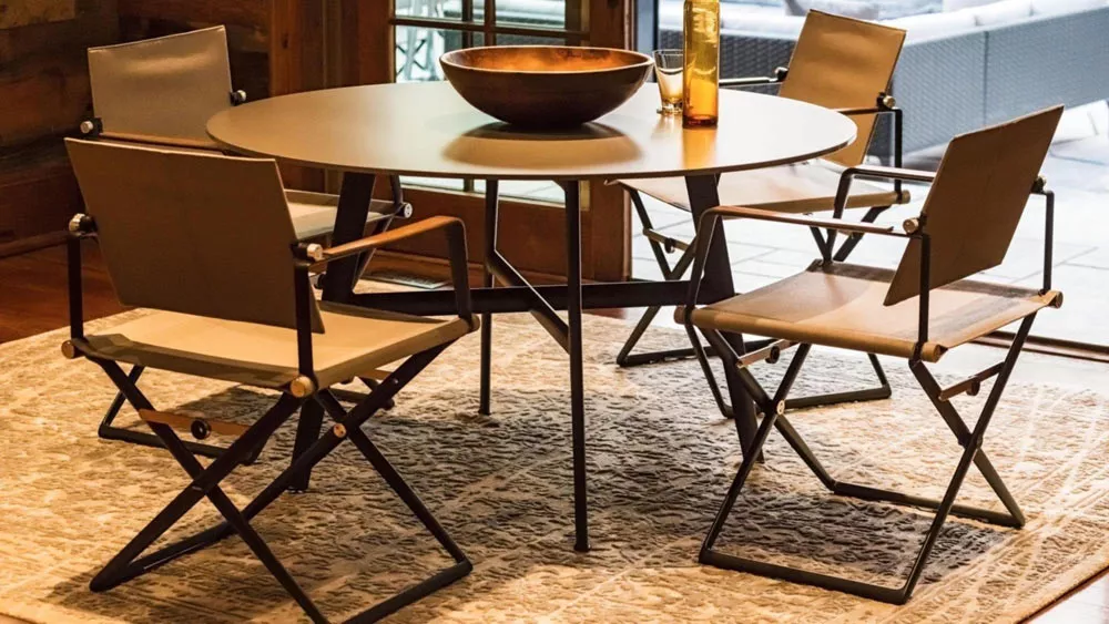 Dedon Seax Esstisch rund mit vier Stühlen auf einem Teppich in einem gemütlichen Raum mit Holzschale und Flasche auf dem Tisch