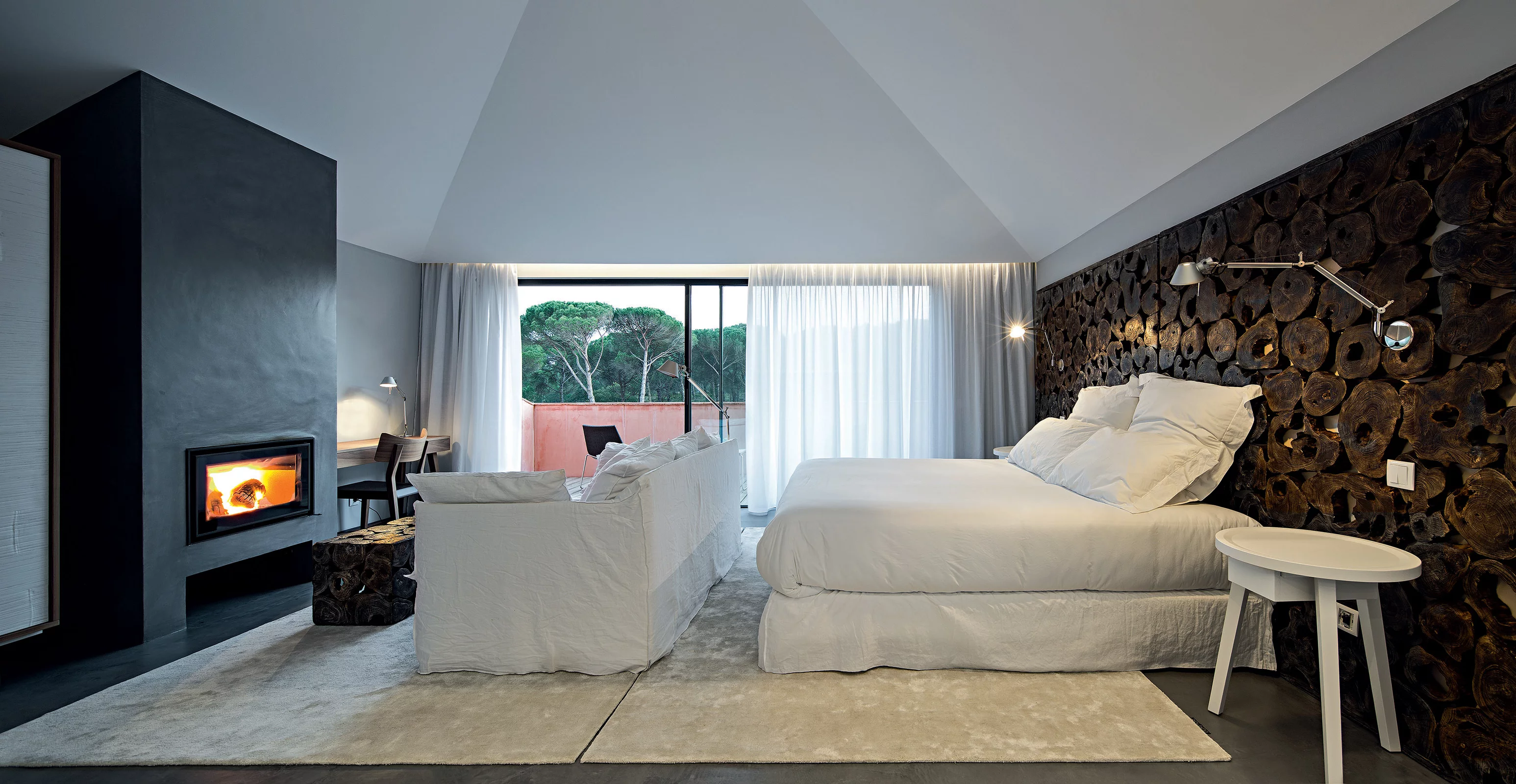 Ein modernes Schlafzimmer mit Gervasoni Möbeln und einem Kamin im Hintergrund große Fenster bieten einen Blick auf die Natur