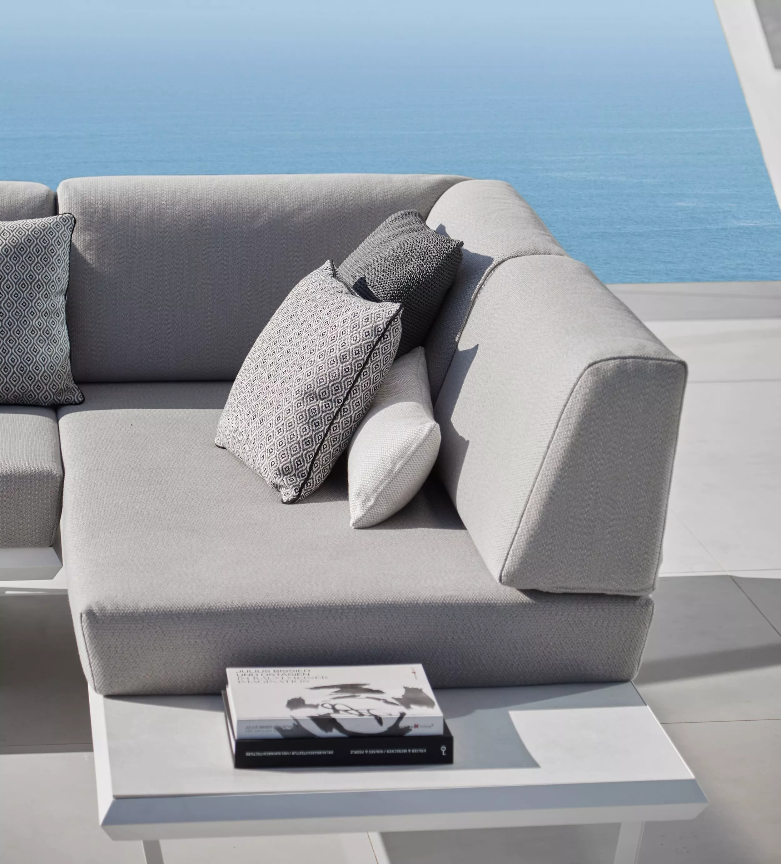 Solpuri Boom Sofa in Grau mit Kissen auf einer Terrasse mit Meerblick und einem Buch auf dem Tisch Mood Bild