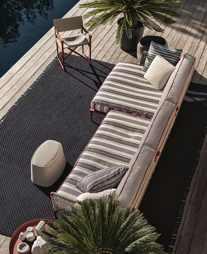 B&B Italia Ribes Outdoor Lounge auf einer Terrasse neben einem Pool mit Pflanzen und einem Beistelltisch mit Getränken und Gläsern im Freien.