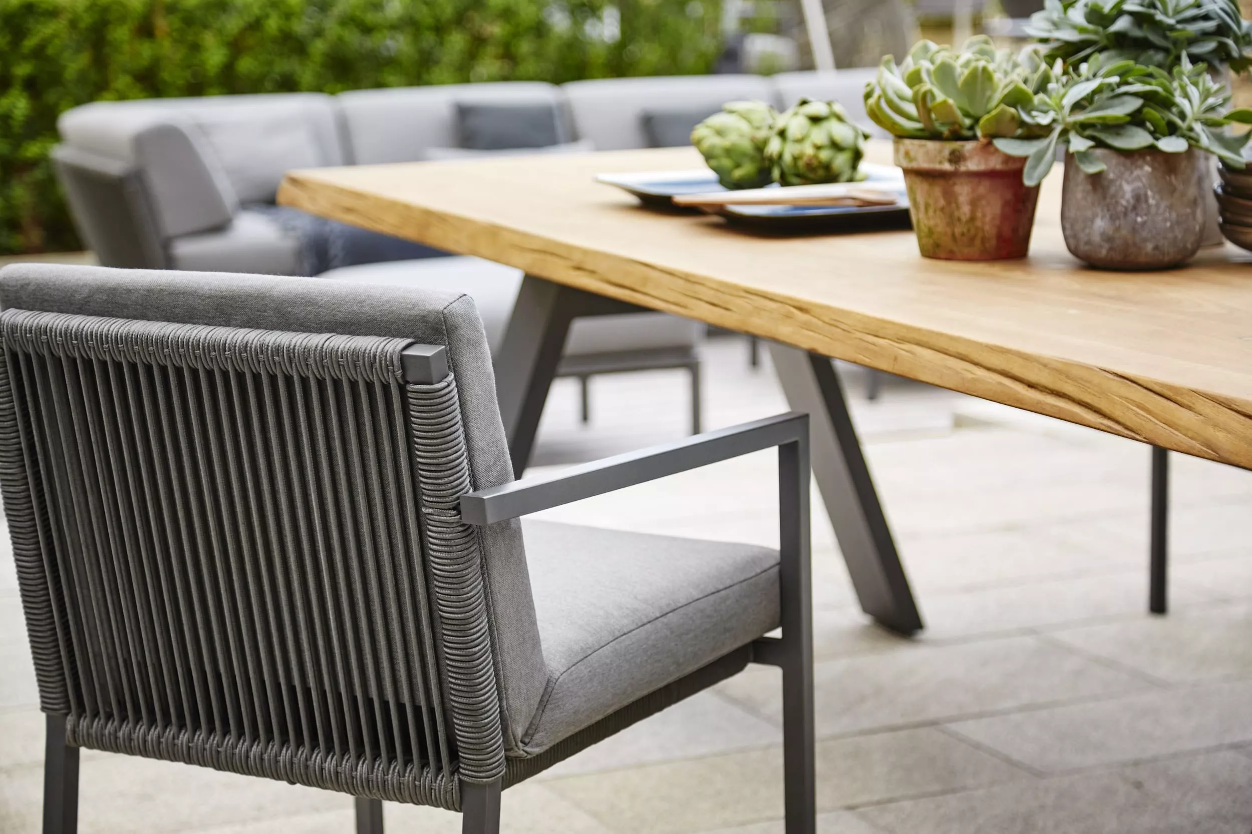 Solpuri Club Ambiente Timber Essbereich im Freien mit grauen Stühlen und Holztisch dekoriert mit Pflanzen und Artischocken in einem Garten.