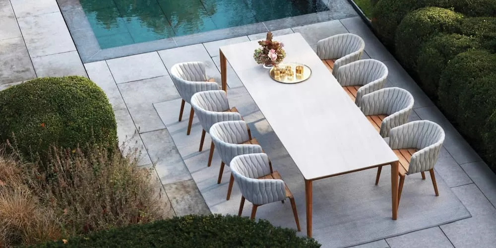 Essgruppe von Villa Schmidt mit weißem Tisch und acht grauen Stühlen auf einer Terrasse neben einem Pool, umgeben von grünen Hecken.