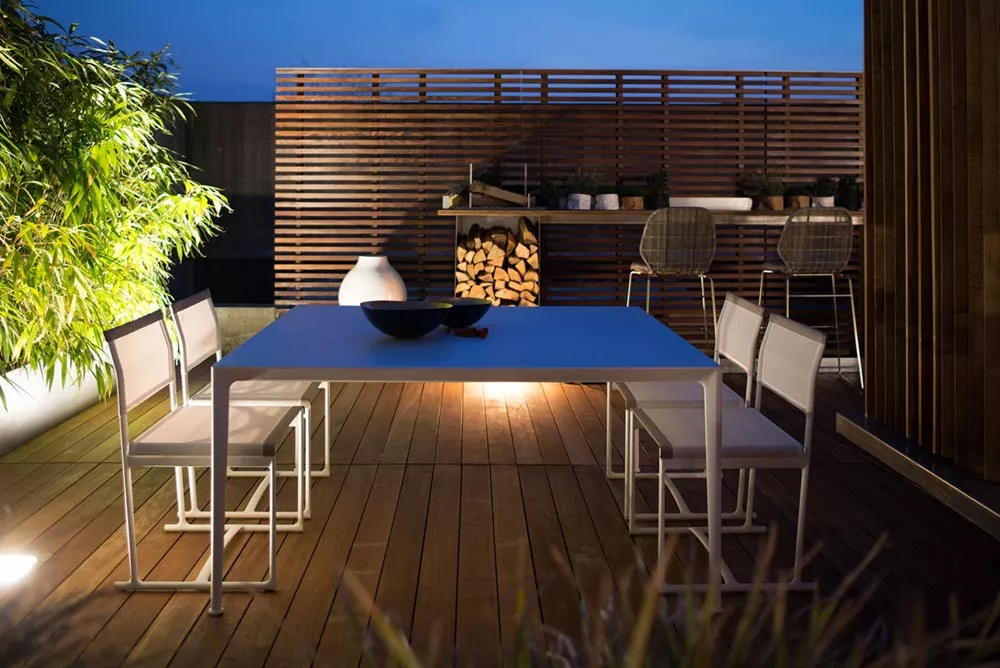 B&B Italia Mirto Outdoor Esstisch auf einer stilvollen Terrasse bei Nacht mit modernen Stühlen und Pflanzen im Hintergrund