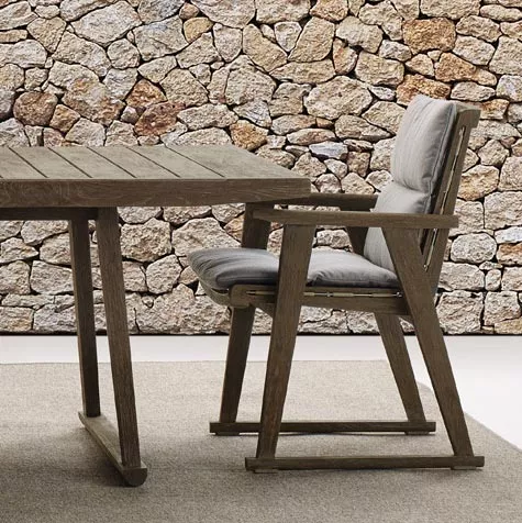 B&B Italia Gio Gartentisch 220 cm und Stuhl aus Holz mit Polsterung vor einer Steinmauer 