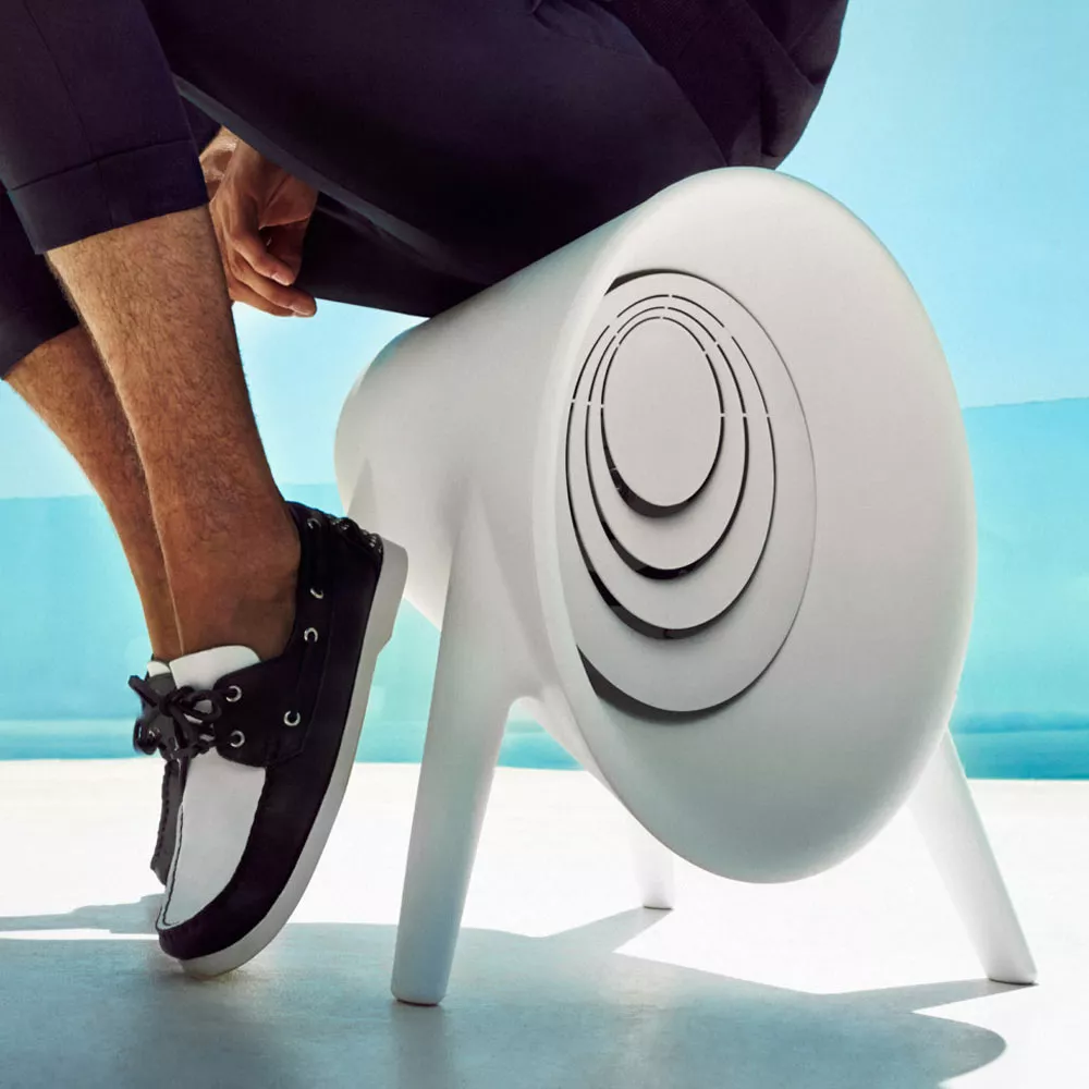 Ein Mann sitzt auf dem Vondom Bum Bum Gartenhocker mit Bluetooth-Soundsystem und Akku in einer modernen Umgebung.