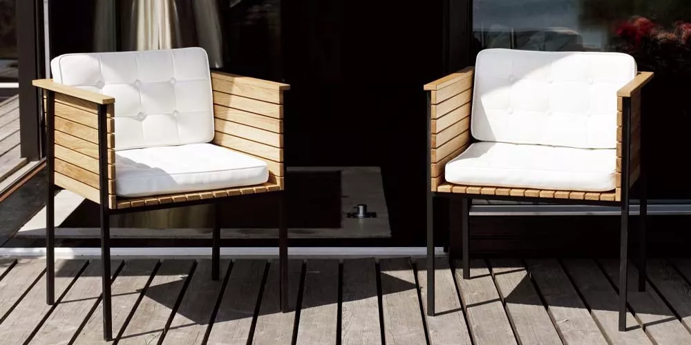 Zwei Skargaarden Häringe Stühle mit weißen Polstern auf einer Holzterrasse vor einer dunklen Glasfassade.