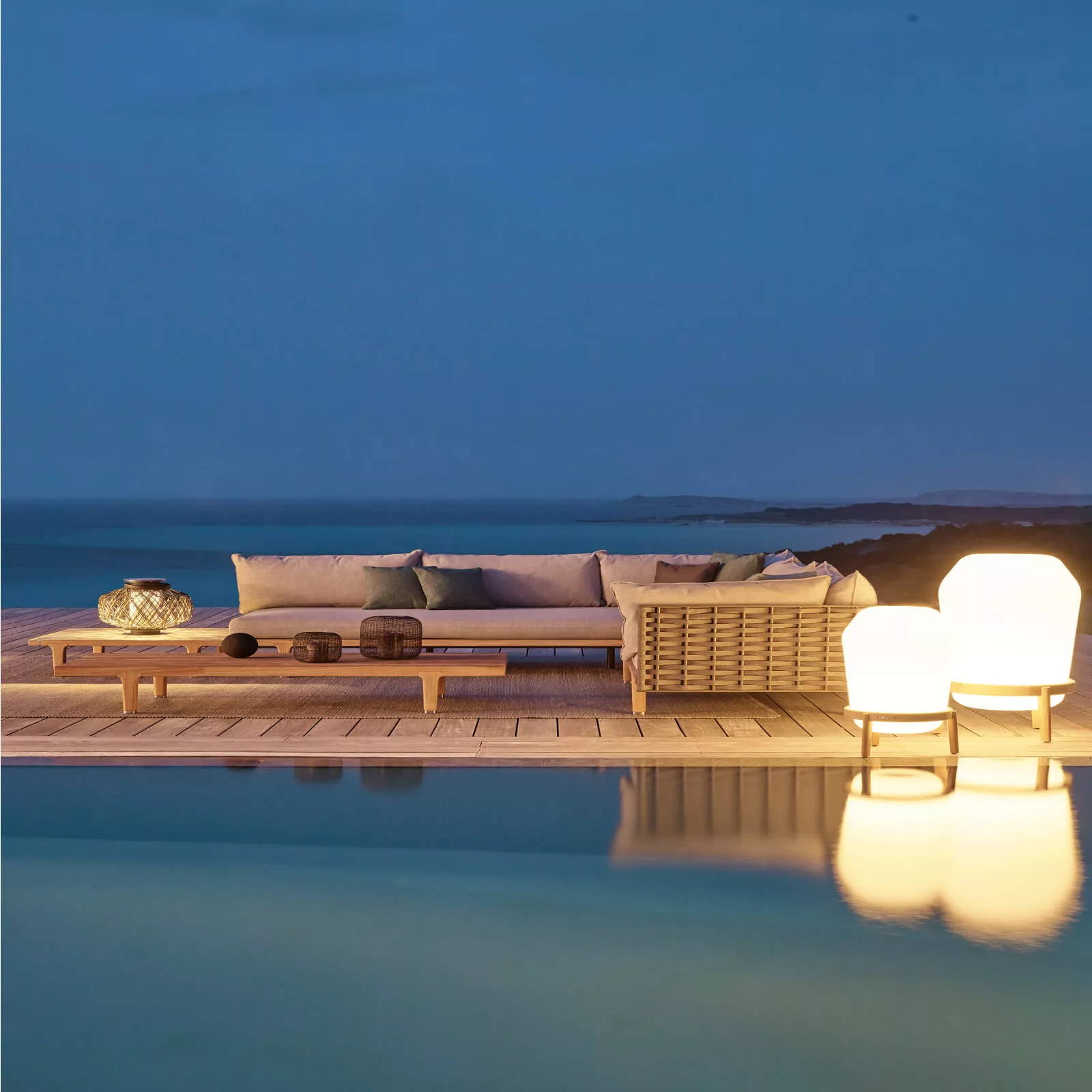 Dedon Sealine Sofa und Couchtisch auf einer Terrasse am Meer bei Dämmerung mit dekorativen Lampen und Kissen im Hintergrund 