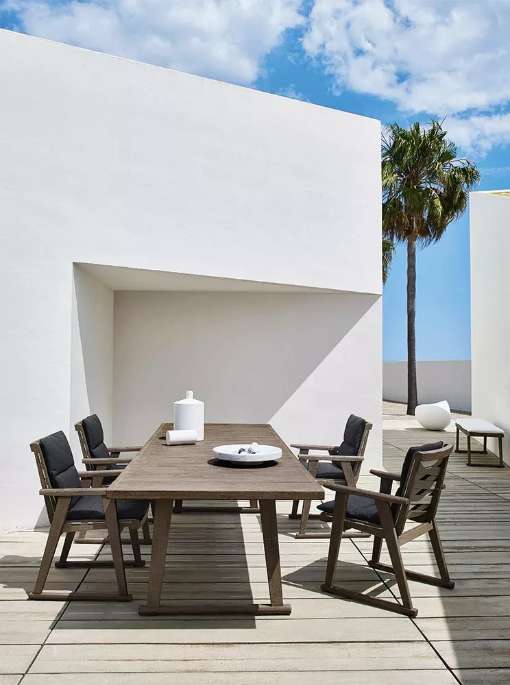 B&B Italia Gio Gartentisch 280 cm mit sechs Stühlen auf einer Terrasse mit weißer Wand und Palme im Hintergrund bei sonnigem Wetter