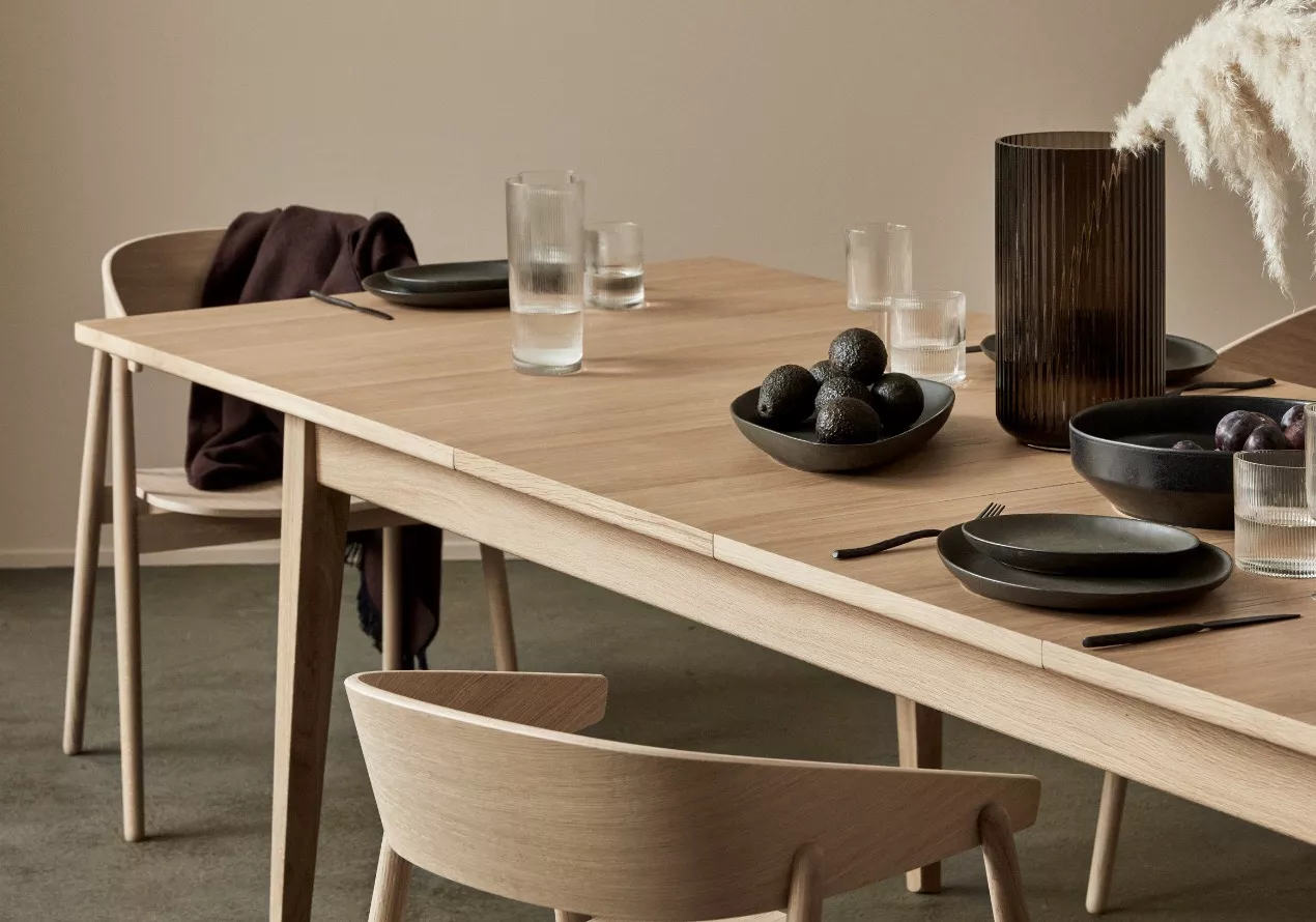 Holztisch von Villa Schmidt in heller Eiche mit schwarzem Geschirr und Gläsern, aufgestellt in einem minimalistischen Raum.