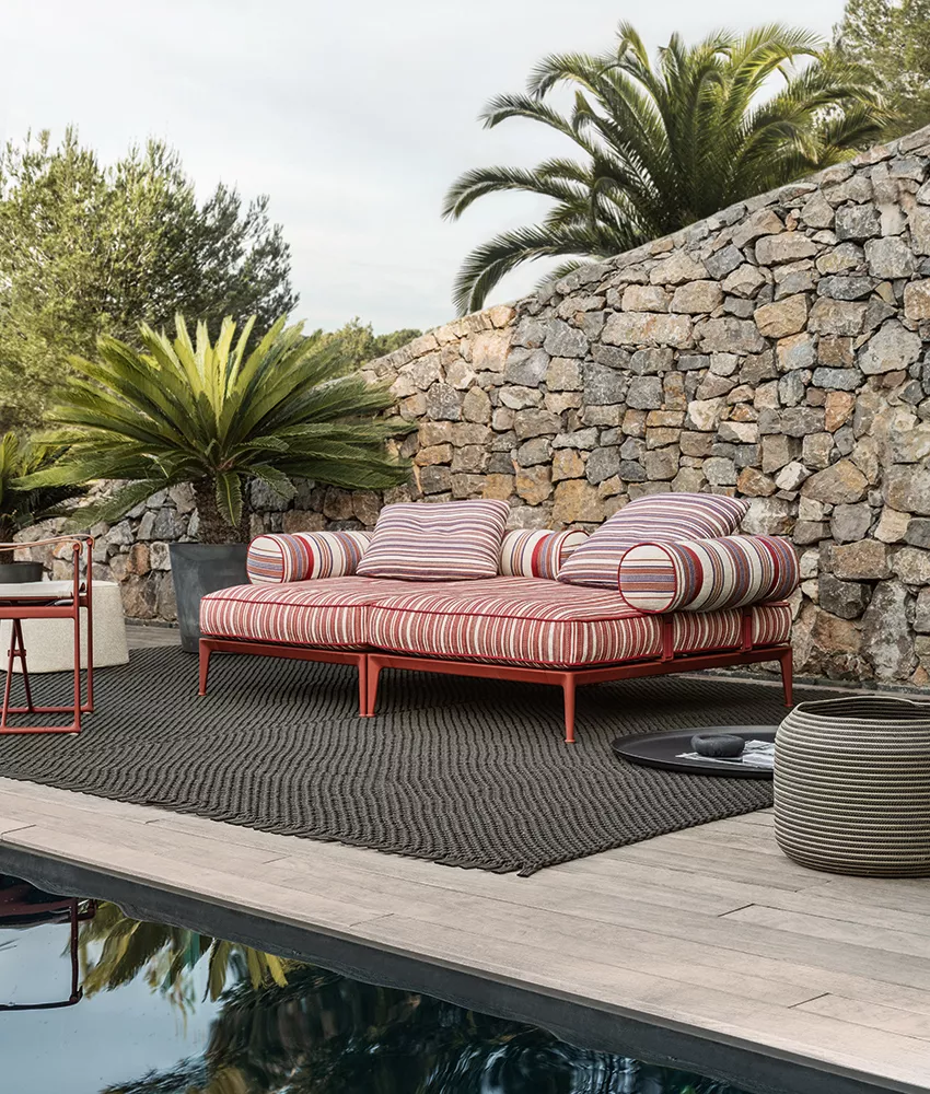 B&B Italia Ribes Outdoor Lounge in einem Garten neben einem Pool mit Steinmauer und Palmen im Hintergrund 